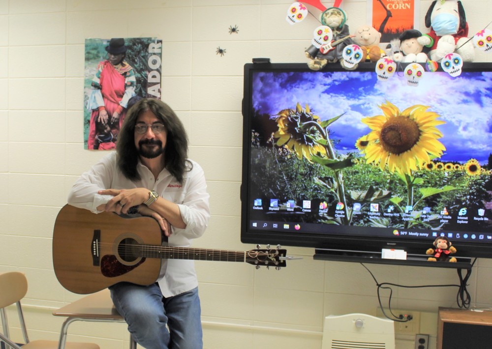 Mr. David Alexander poses with a guitar, while sitting in his classroom at Heritage High School. 